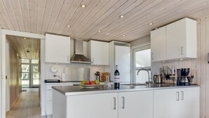 Una cocina moderna con armarios blancos, una campana extractora de acero inoxidable y una isla grande con una botella de vino y fruta.