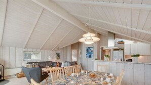 A spacious dining area with a high ceiling and wooden beams, featuring a large table with a floral tablecloth and multiple chairs.
