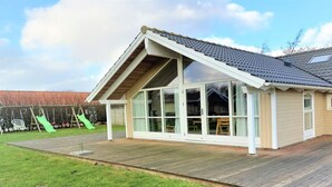 A modern house with a large glass window area, a wooden deck, and a green slide in the background.