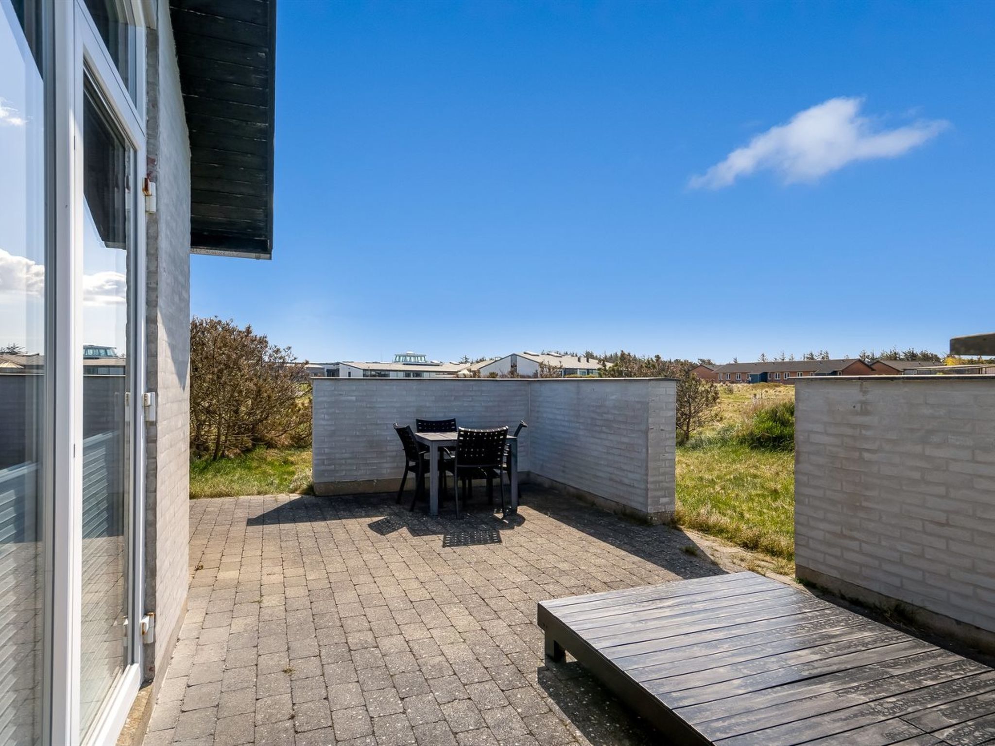A patio area with a table and chairs, a wooden bench, and a view of the surrounding landscape.