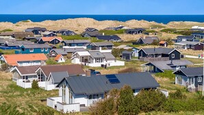 Un quartier résidentiel situé sur la côte, avec des maisons aux toits de différentes formes et de couleurs variées, entouré de dunes et donnant sur la mer.