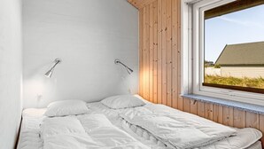 Une chambre avec un plafond en bois, des murs blancs, une grande fenêtre et deux lampes de chevet.