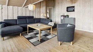 En moderne stue med en krombækssofa, et sofabord, en lænestol og et fjernsyn monteret på væggen.