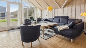 En moderne stue med sofa, lænestole, sofabord og en hængende lampe.