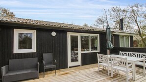 Une terrasse en bois avec une table et des chaises, un canapé en osier et un parasol.