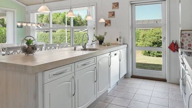 Una cocina moderna con armarios blancos, una isla grande, luces colgantes y vistas al exterior.