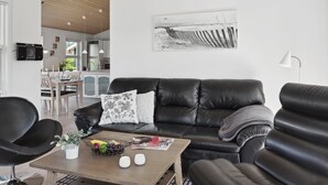 Una sala de estar moderna con un sofá de cuero negro, una mesa de centro de madera con frutas y una revista, y un diseño minimalista.