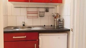 Kompakti keittiö, jossa on punaiset kaapit, valkoinen jääkaappi ja musta työtaso.
