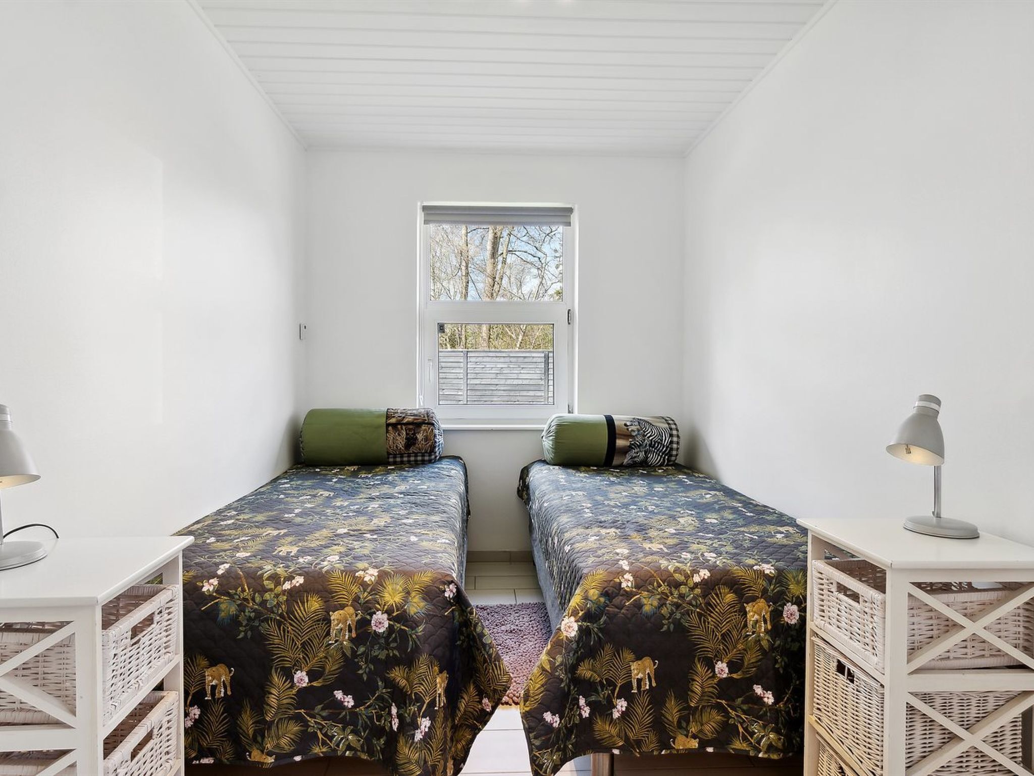 Une petite pièce lumineuse, avec deux lits simples, une fenêtre et un plafond blanc.