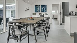 Una cocina moderna con una isla central, un área de comedor con una mesa larga y sillas, y vistas al exterior.
