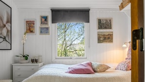 A bedroom with a large window, a bed with patterned bedding, a bedside table with a vase and glasses, and wall art. - "Hellevi" -  from the sea by Interhome (Hals)