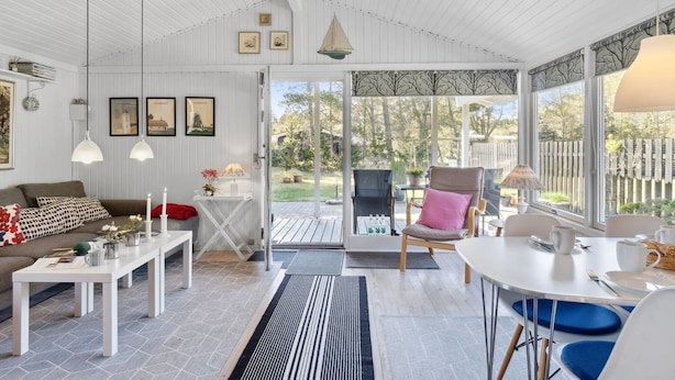 A spacious living area with a white ceiling, a sofa, a coffee table, and a dining table with chairs. There is a large window providing a view of the outdoors. - "Hellevi" -  from the sea by Interhome (Hals)