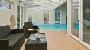 A covered patio area with a pool, wicker furniture, and a glass table.