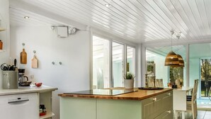 A modern kitchen with a large island, white cabinetry, and a dining area with a view of the outdoors.