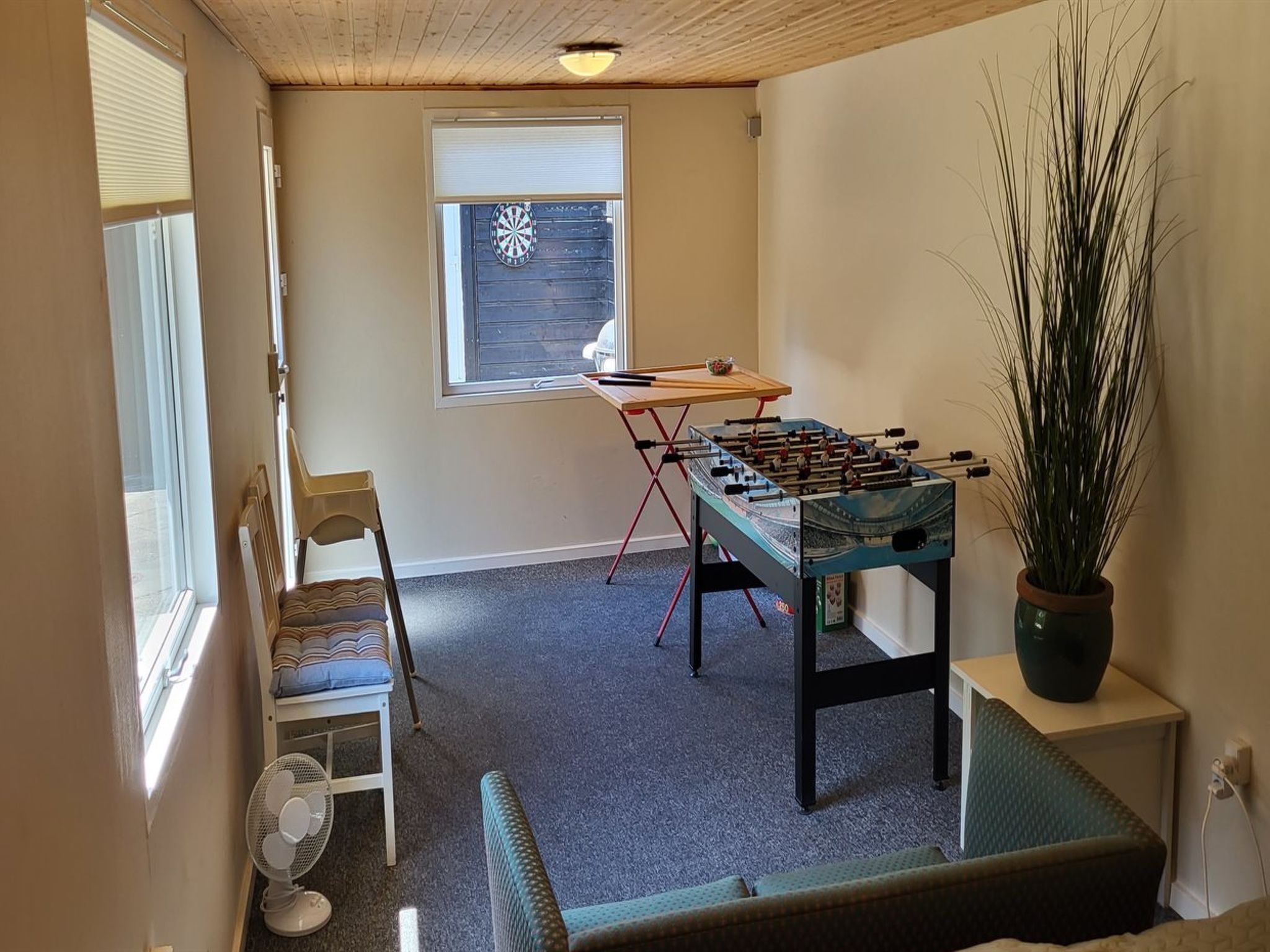 Una habitación con una mesa de futbolín, una silla, una mesita, una ventana y una planta en maceta.