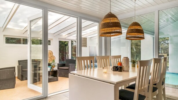 A modern dining area with a white table and chairs, large windows, and wicker pendant lights.