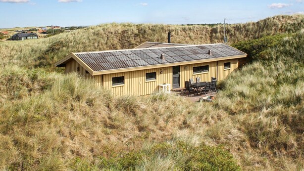 A single-story building with a flat roof, surrounded by tall grass and dunes.