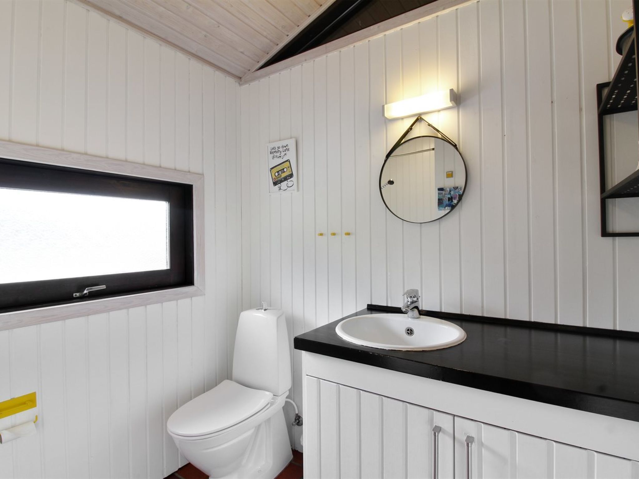 Une salle de bain avec des toilettes blanches, un lavabo doté d’un plan-vasque noir et un miroir avec un éclairage au-dessus.