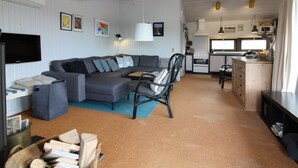 A modern living room with a grey sectional sofa, a black chair, and a small table. A kitchen is visible in the background with white cabinets and a stove.