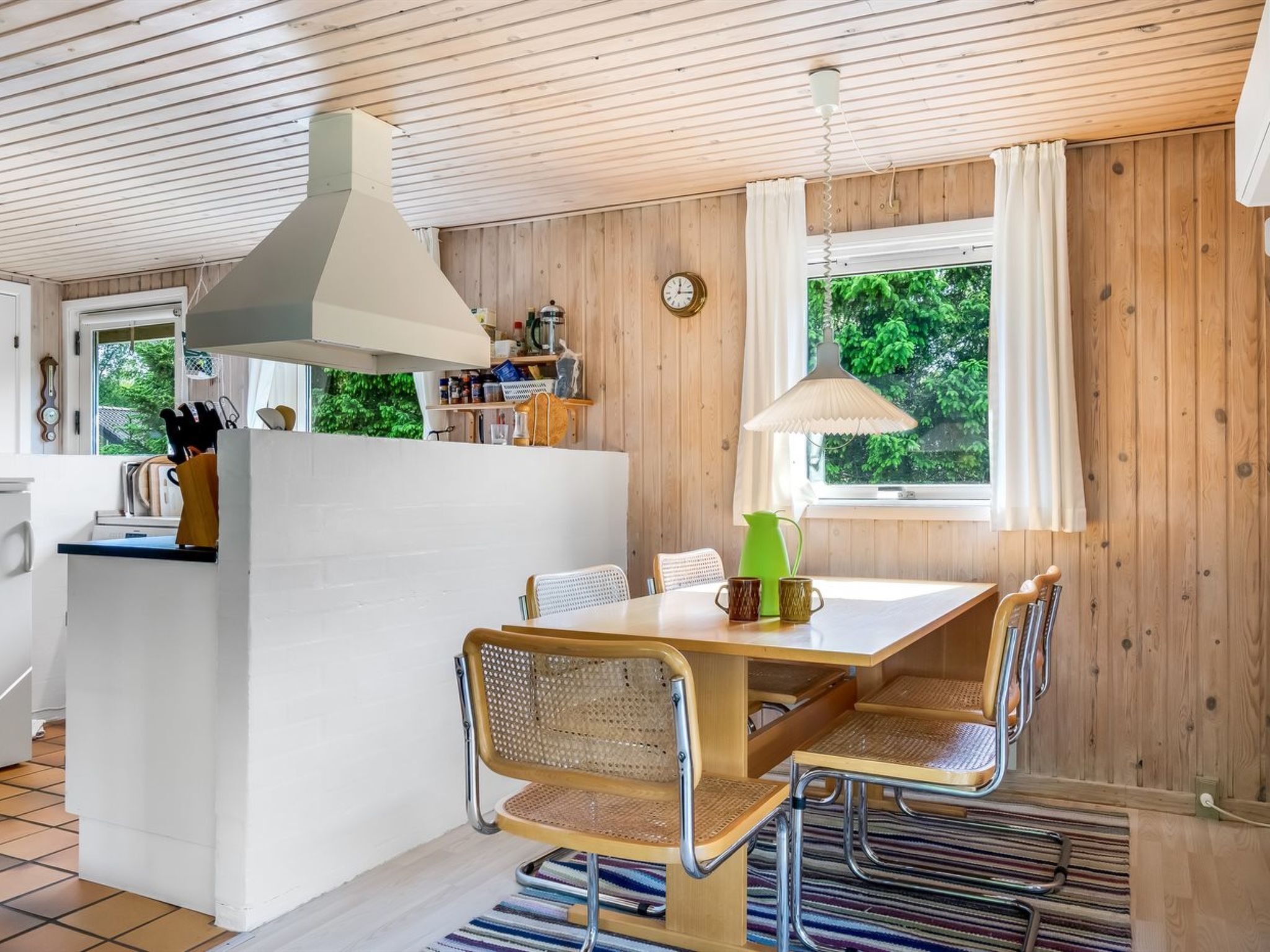 Une cuisine chaleureuse avec un îlot central, des murs en bois et une fenêtre donnant sur un paysage verdoyant.
