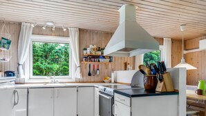 A compact kitchen with white cabinets, a stove, and a large window offering a view of greenery. - "Myrna" - 300m from the sea by Interhome (Hals)