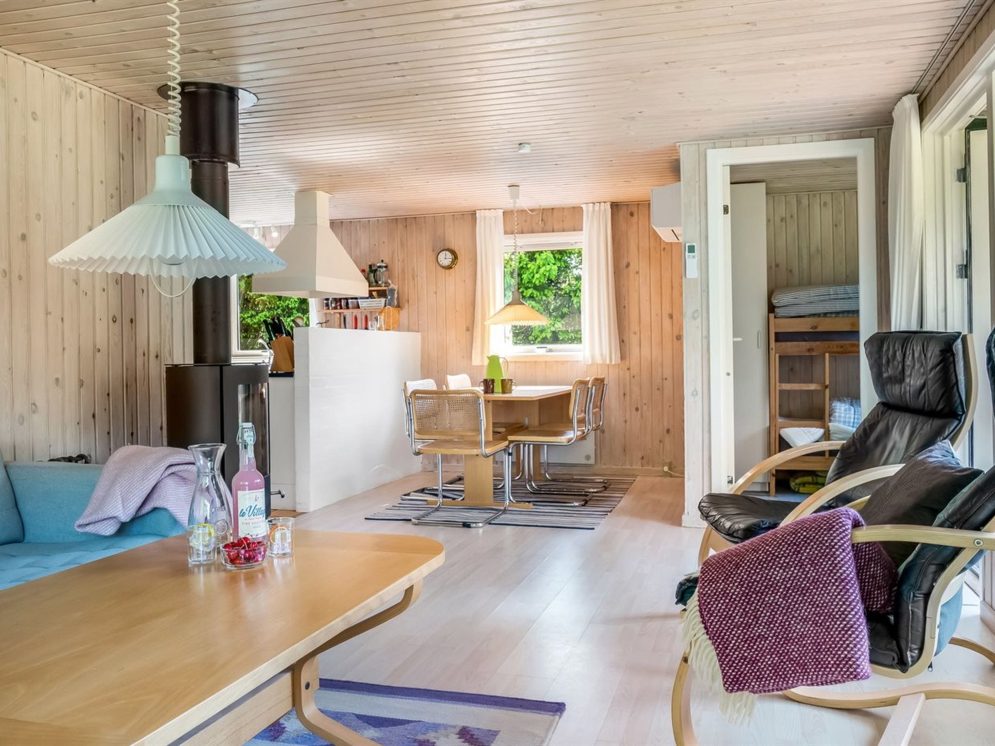 L’intérieur chaleureux d’un chalet avec un coin repas en bois, un canapé, une table avec des boissons et un lit superposé avec une chaise.