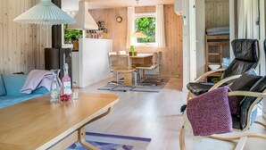 A cozy cabin interior with a wooden dining area, a sofa, a table with drinks, and a bunk bed with a chair. - "Myrna" - 300m from the sea by Interhome (Hals)