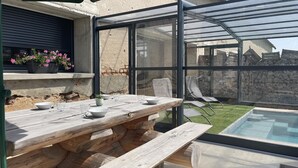 A wooden picnic table with a glass enclosure, a small pool, and a stone wall in the background.