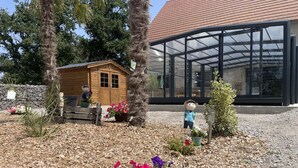 A garden area with a wooden cabin, a greenhouse, and a small statue.
