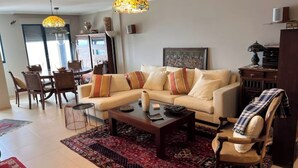 Un salon avec un canapé, une table basse et des fauteuils. On y trouve également une table à manger avec des chaises et un tapis.