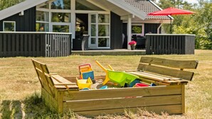 A wooden play area with a bench, a small shed, and a house with a red roof in the background.