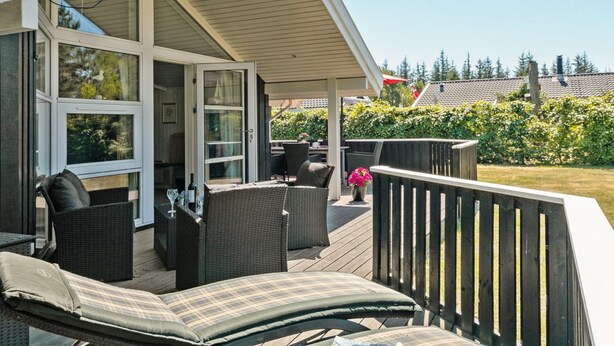 A covered outdoor deck with wicker furniture and a lounge chair.