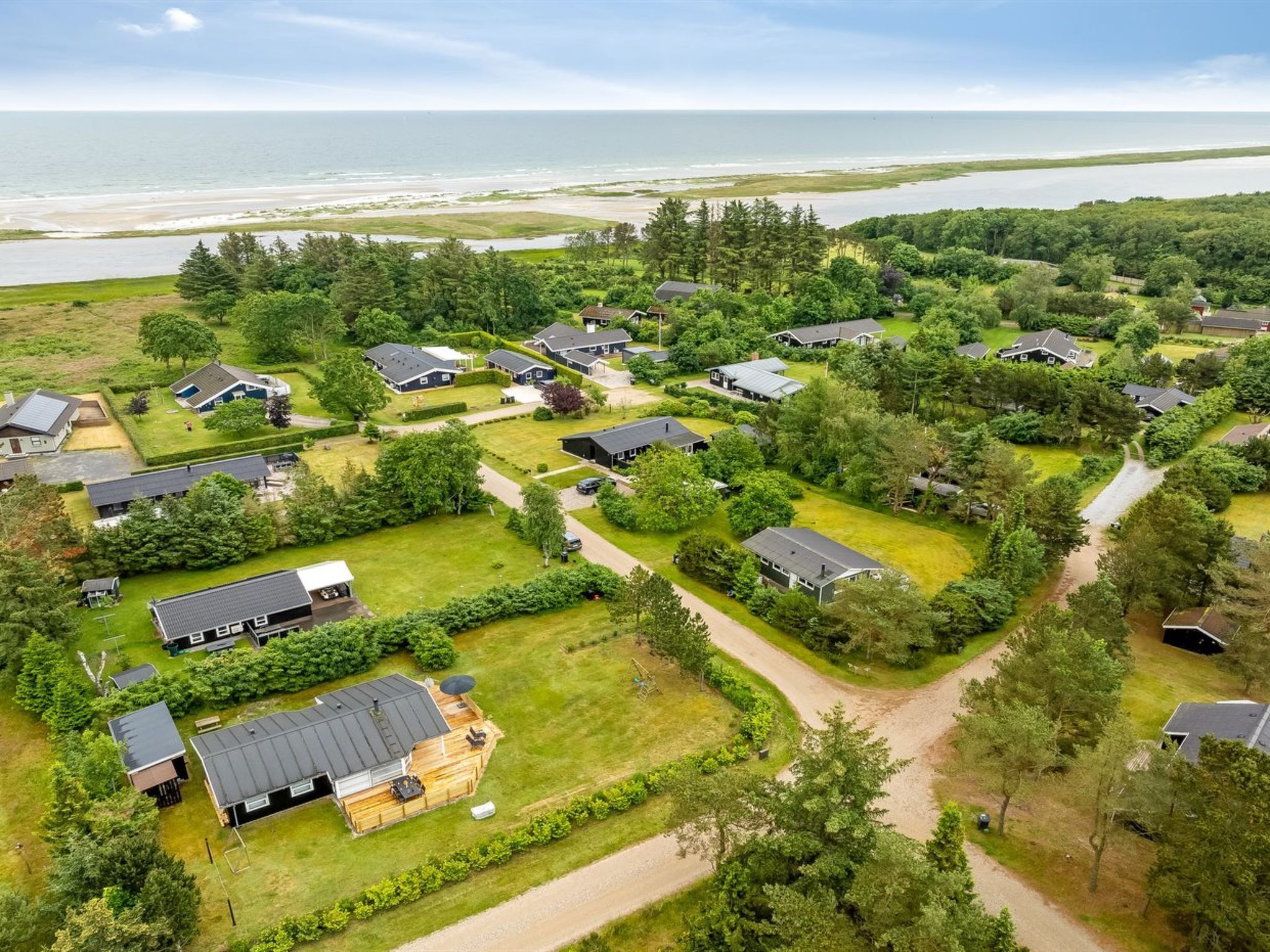 An aerial view of a residential area with houses, green lawns, and a beach in the background.