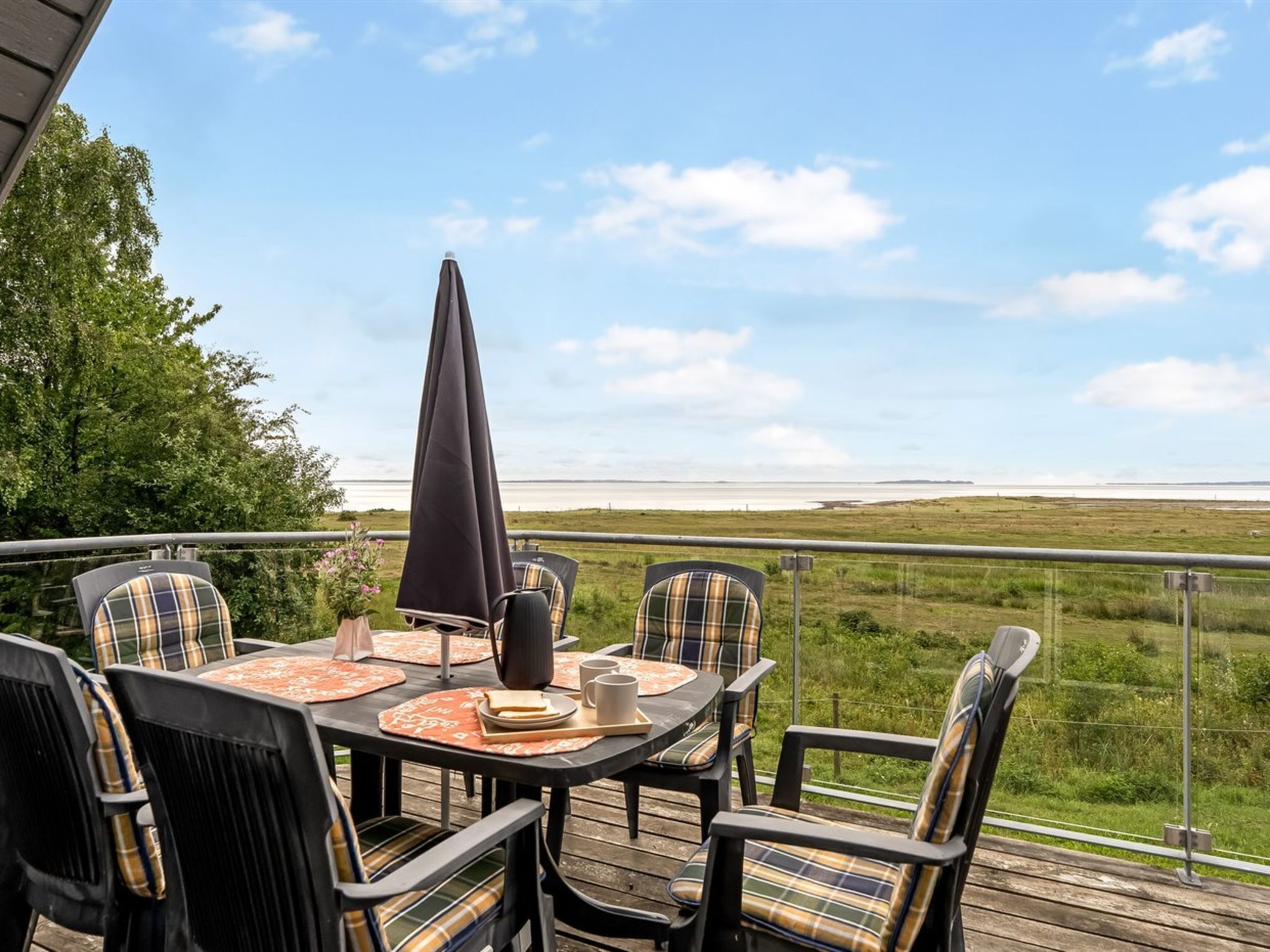 A deck with a table and chairs, overlooking a grassy field and a body of water.