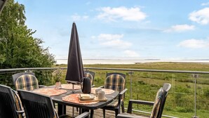 A deck with a table and chairs, overlooking a grassy field and a body of water.