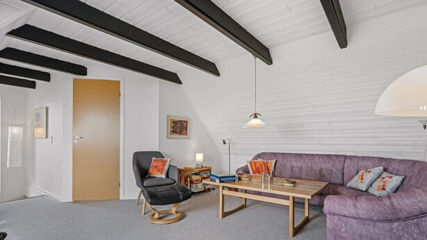 A modern living room with a high ceiling, a wooden floor, a purple sofa, a black leather chair, and a coffee table.