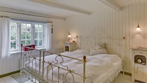 A white paneled bedroom with a metal bed frame, a bedside table with a lamp, and a window with curtains. - "Clausina" - 600m from the sea by Interhome (Bredebro)