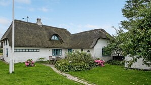 A traditional thatched-roof house with a white exterior, a small garden with pink flowers, and a clear sky. - "Clausina" - 600m from the sea by Interhome (Bredebro)