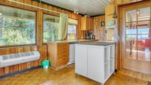 Moderni keittiö, jossa on puiset kaapit, keskeinen keittiösaareke ja suuri ikkuna, josta avautuu näkymä ulos.