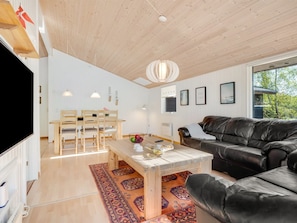 Una sala de estar moderna con techo de madera, un sofá de cuero negro, una mesa de comedor de madera y un ventanal grande.
