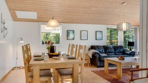 Een ruime woonkamer met een houten plafond, een eettafel met stoelen, een zwarte leren bank en een salontafel.