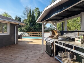 Un espacio al aire libre techado con una parrilla, una piscina y una terraza de madera.