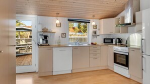 Een moderne keuken met een houten plafond, witte kastjes, een vaatwasser, een fornuis en een raam met uitzicht op een terras.