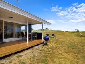 A modern house with a covered patio, a barbecue grill, and outdoor seating.