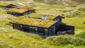 Une maison moderne avec un toit végétalisé, située dans un champ verdoyant, avec une forêt en arrière-plan.