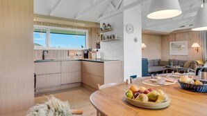 Une cuisine moderne avec des meubles en bois, une table à manger ornée de fruits et un coin salon avec un canapé et une lampe.