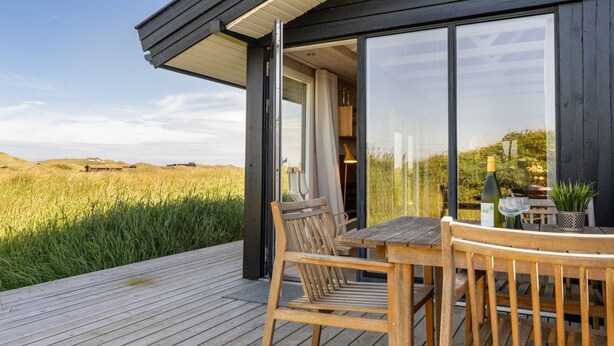 Une terrasse en bois avec une table et des chaises, de grandes fenêtres et une vue sur un champ verdoyant.