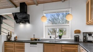 Une cuisine moderne avec des meubles en bois, un lave-vaisselle encastré, une fenêtre avec vue, des luminaires suspendus et une machine à café.