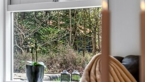 Une pièce dotée d’une grande fenêtre donnant sur une zone boisée. Un pot de fleurs est posé sur le rebord de la fenêtre, ainsi que quelques bocaux en verre.