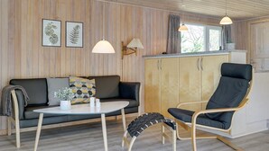 Een knus vertrek met een houten plafond, een bank, een eettafel, een stoel en een kast.